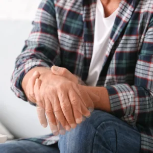 Man wearing plaid shirt holding his wrist while his hand is shaking.