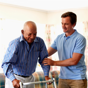 A male caregiver helping an older man walk with his walker.