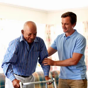 A male caregiver helping an older man walk with his walker.