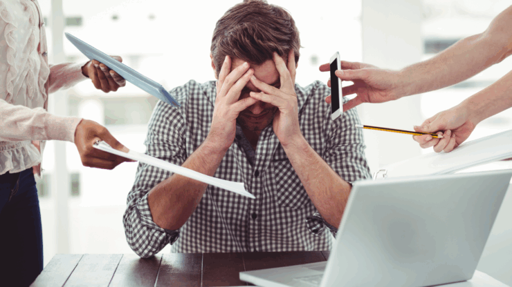 Man with hands on his face, surrounded by paper and pens. He looks overwhelmed.